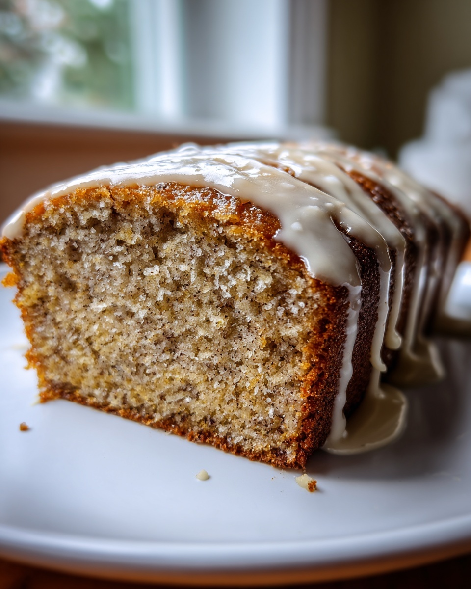 A close-up of a thick slice of moist eggnog bread topped with a sweet vanilla glaze dripping down the sides.