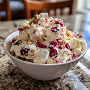 A close-up of a fluffy white cranberry salad mixed with bright red cranberries, marshmallows, and chopped nuts in a white bowl.