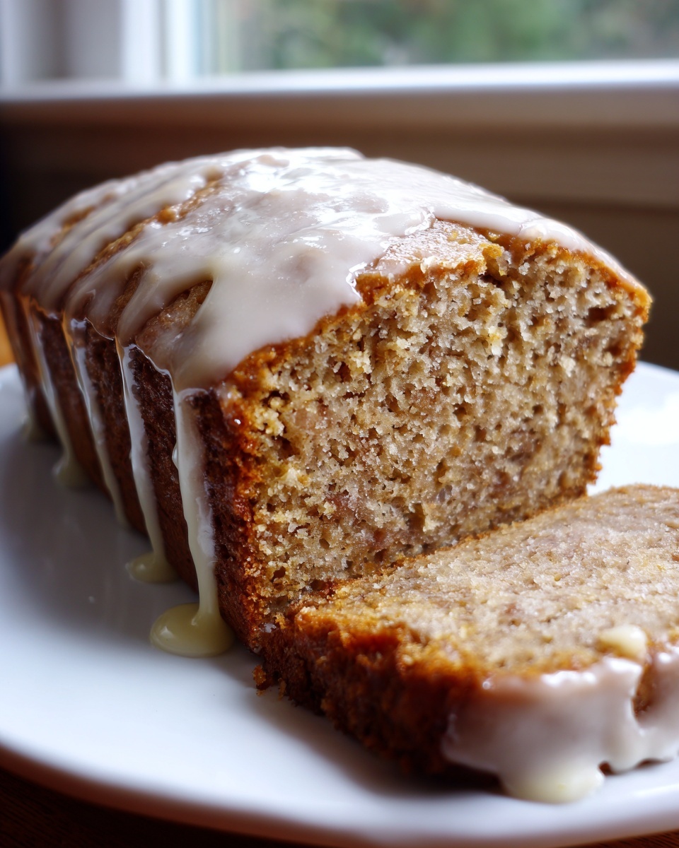 Close-up of a moist eggnog bread loaf, drizzled with white glaze, with one slice cut and resting beside it.