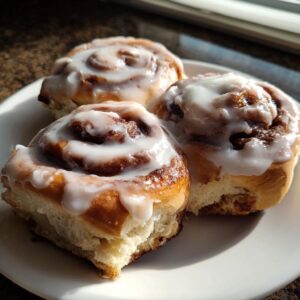 Three freshly baked cinnamon rolls recipe swirls topped with thick white icing on a white plate.