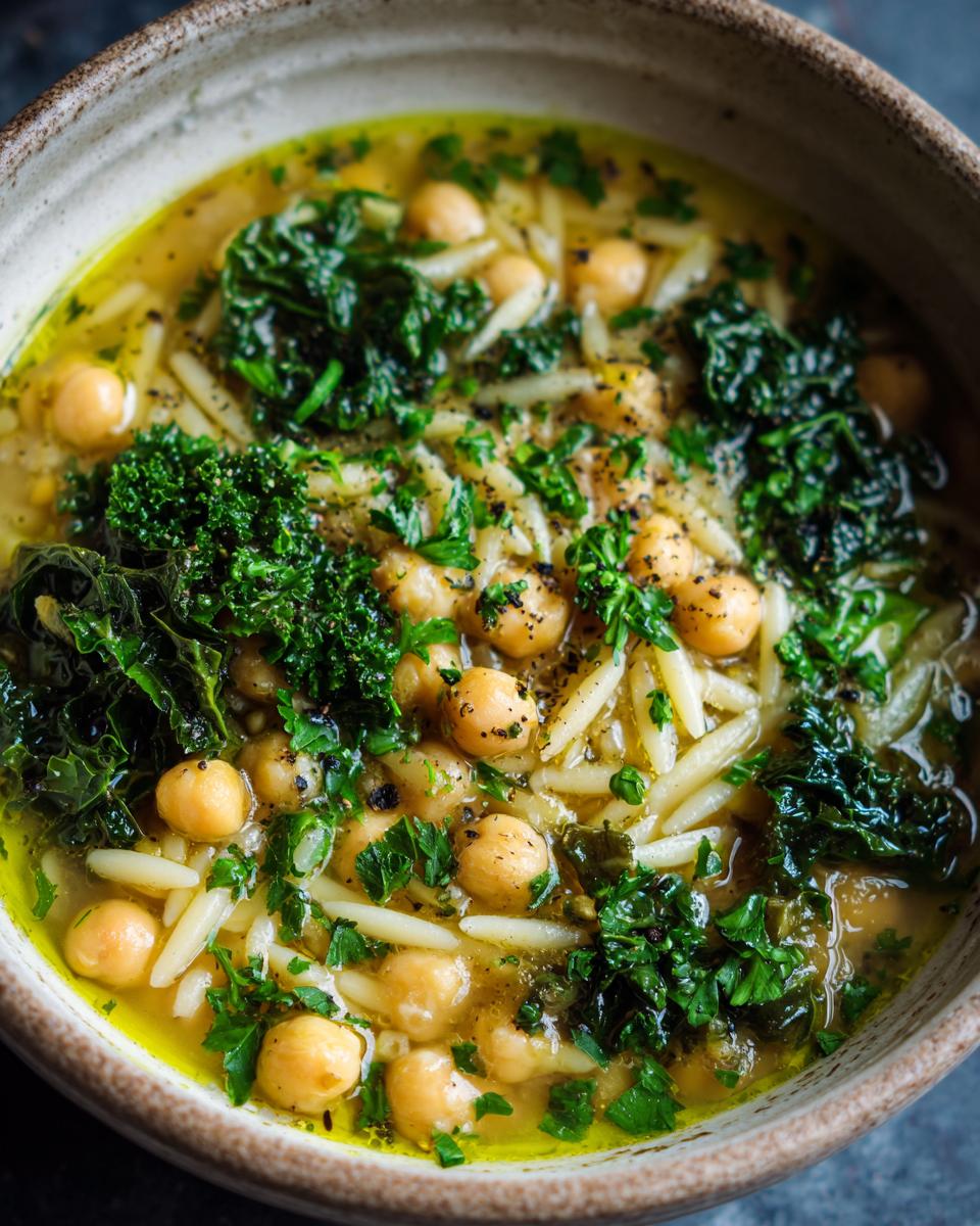 Close-up of a bowl of vibrant greek chickpea soup featuring chickpeas, orzo pasta, and dark green kale.