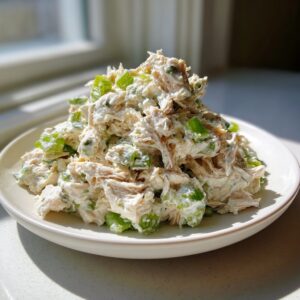 A mound of creamy high protein chicken salad mixed with chopped green celery served on a white plate.