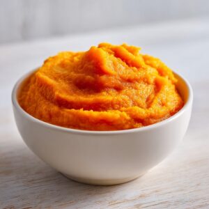 A close-up of vibrant orange homemade pumpkin puree mounded high in a small white bowl.