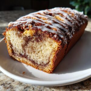 A close-up of a freshly baked cinnamon bread loaf, showing the swirl interior and white icing drizzle.