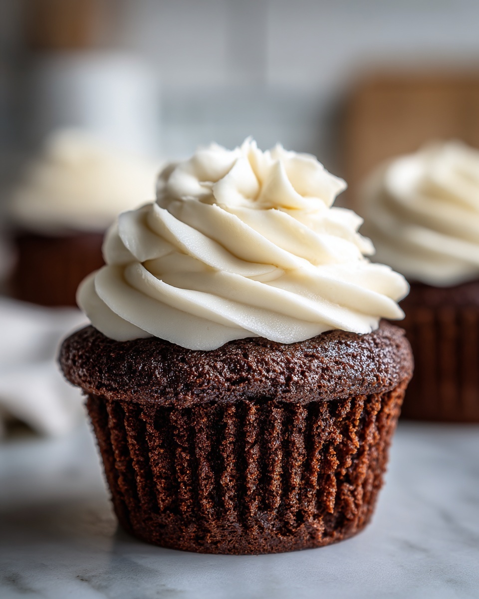 Close-up of a dark, moist gingerbread cupcakes topped with a swirl of white cream cheese frosting.