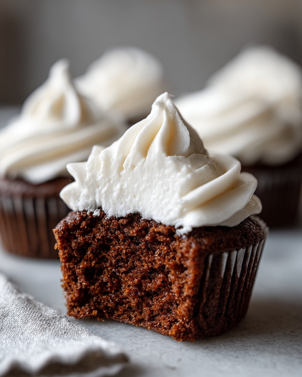Close-up of a gingerbread cupcakes cut in half showing the moist crumb and white cream cheese frosting.