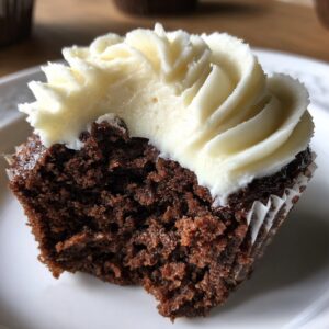 Close-up of a gingerbread cupcakes cut in half showing moist dark cake and thick swirl of white frosting.