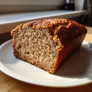 A thick slice of moist protein banana bread with a dark golden crust, sitting on a white plate.