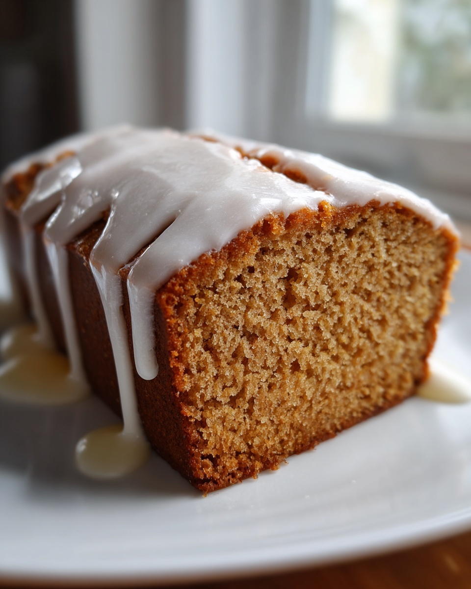 Close-up of a moist slice of eggnog bread topped with thick white glaze dripping down the sides.
