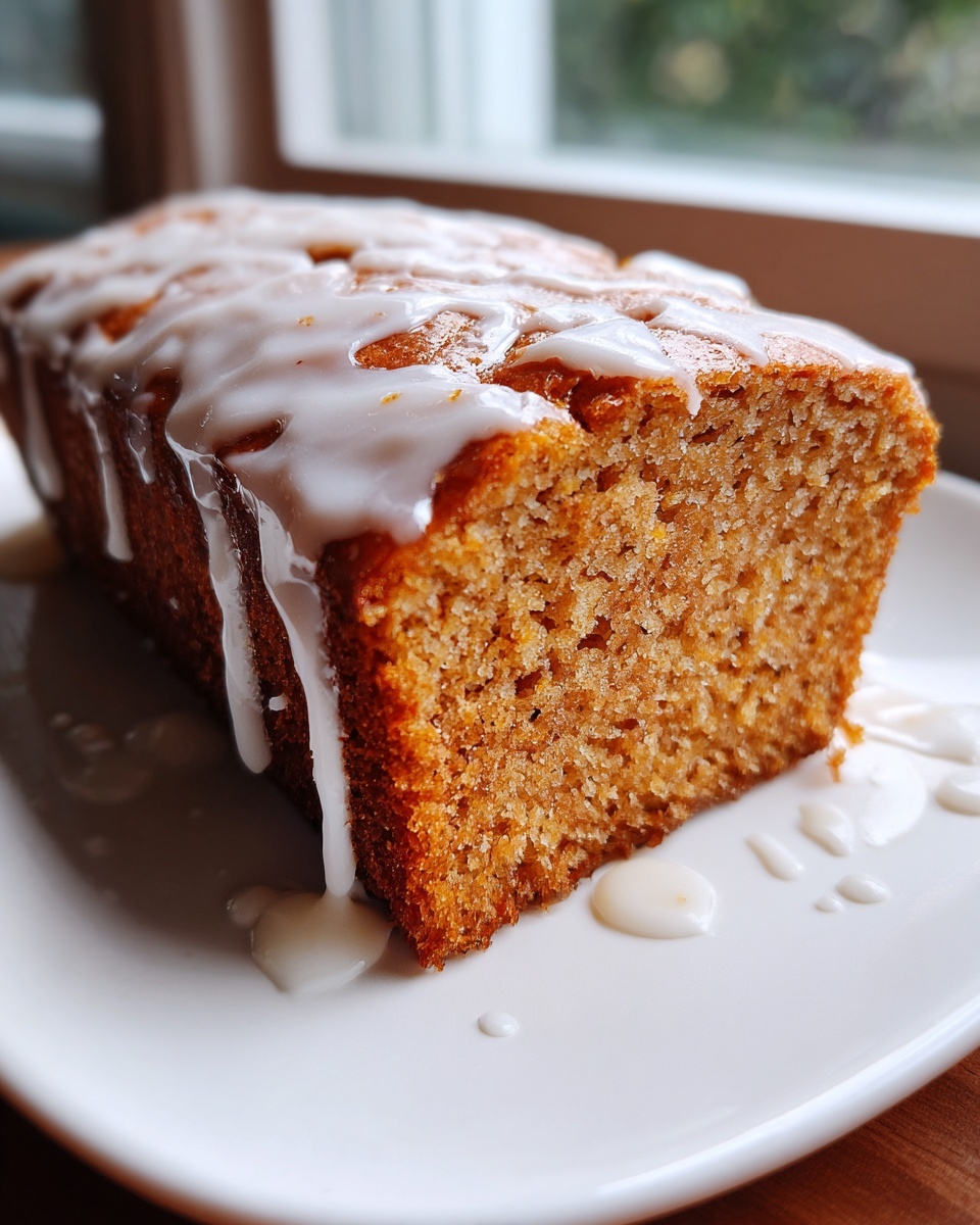 Close-up of a moist slice of eggnog bread topped with a thick, dripping vanilla glaze.