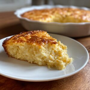 A thick slice of creamy, golden-brown topped corn pudding custard on a white plate.