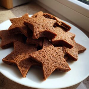 A pile of perfectly shaped, un-iced star gingerbread cookies resting on a white plate.