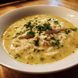 Close-up of a white bowl filled with creamy chicken orzo soup, topped with shredded chicken and fresh parsley.