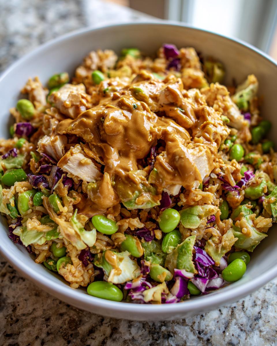 Close-up of a bowl filled with crispy rice salad, topped with chicken pieces and a generous drizzle of peanut sauce.