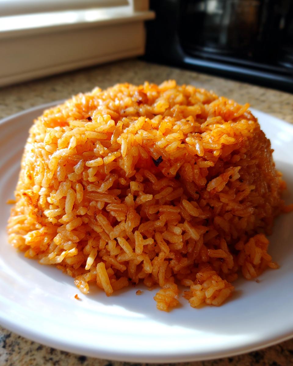 A perfectly molded mound of vibrant orange, fluffy jollof rice served on a white plate, showing individual grains.