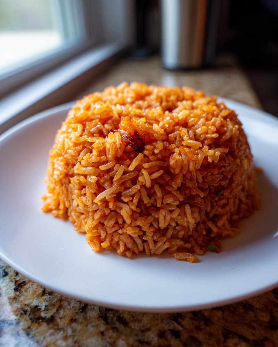 A perfectly molded mound of vibrant orange jollof rice served on a white plate.